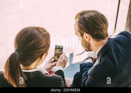 Rear view of business people looking in phone while sitting outdoors Stock Photo