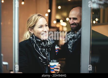 Smiling mid adult businesswoman and businessman leaving cafe Stock Photo
