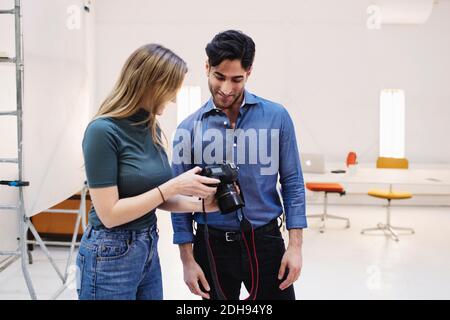 Male and female bloggers watching photographs on digital camera in office Stock Photo