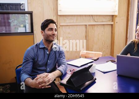 Smiling young man looking away while sitting at desk in office Stock Photo