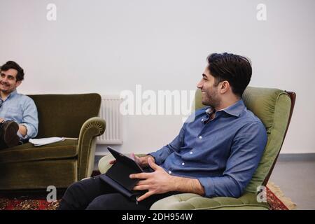 Young man looking at colleague while sitting on armchair in creative office Stock Photo