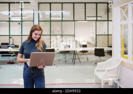 Happy young woman using laptop in creative office Stock Photo