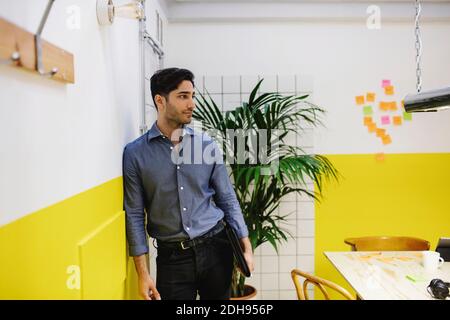 Thoughtful young man leaning on wall in creative office Stock Photo