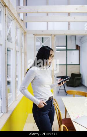 Young woman holding smart phone while standing in creative office Stock Photo