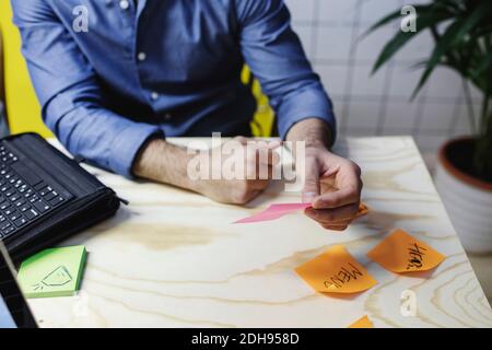 Midsection of male holding adhesive note at wooden desk Stock Photo