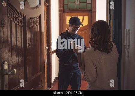 Rear view of customer holding package while delivery man using phone at doorstep Stock Photo