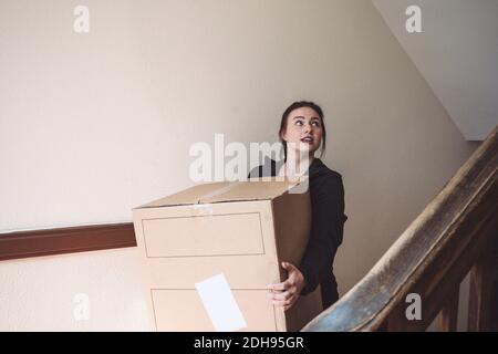 Delivery woman with cardboard box looking up against wall Stock Photo