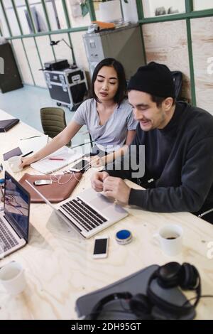 Young woman and man using laptop at desk in office Stock Photo