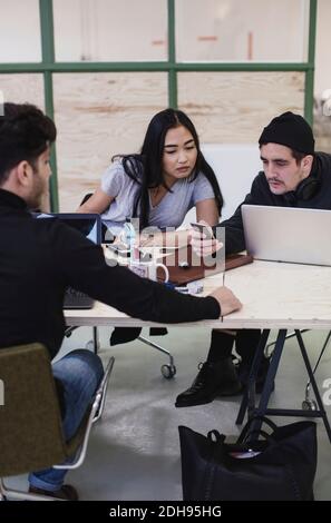 Three colleagues using smart phone at desk in creative office Stock Photo