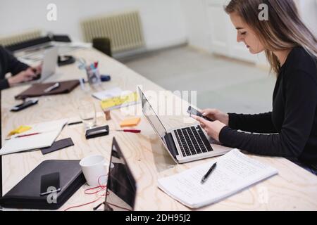 Young woman using smart phone at desk in creative office Stock Photo