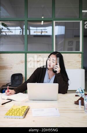 Woman using smart phone at desk in creative office Stock Photo