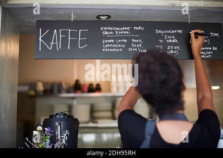 Rear view of waitress writing on blackboard at cafe Stock Photo