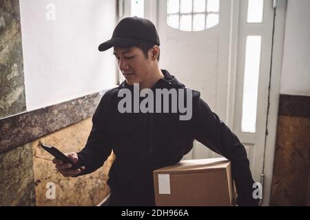 Delivery man using mobile phone while holding package against door Stock Photo