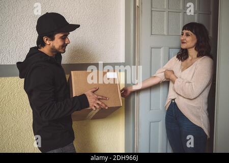 Smiling delivery man with package talking to customer at doorstep Stock Photo
