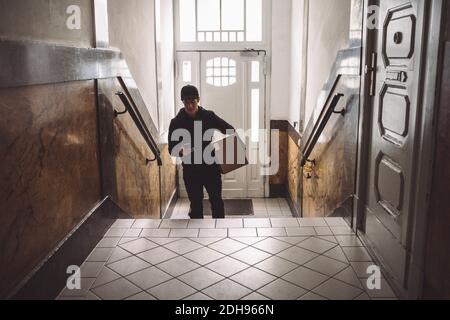Delivery man with package using mobile phone against door Stock Photo