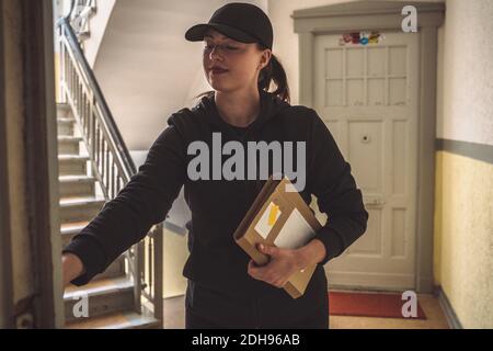 Confident delivery woman with package standing at doorstep Stock Photo