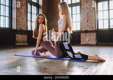Two young women do complex of stretching yoga asanas in loft style class. Stock Photo