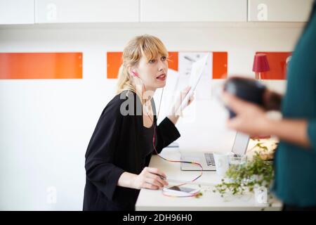 Mid adult businesswoman using hands-free device at table in office Stock Photo