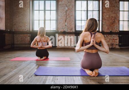 Two young women do complex of stretching yoga asanas in loft style class Stock Photo