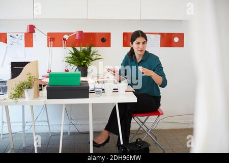 Mid adult businesswoman gesturing while holding digital tablet at table in office Stock Photo