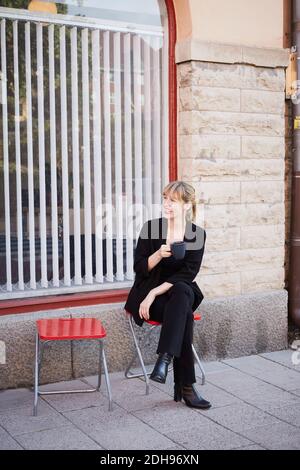 Full length of smiling mid adult businesswoman having coffee while sitting outside office Stock Photo