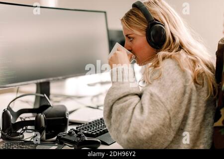 Side view of businesswoman drinking coffee while working on computer in office Stock Photo