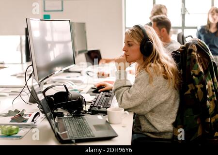 Female colleague looking at computer while working in office Stock Photo