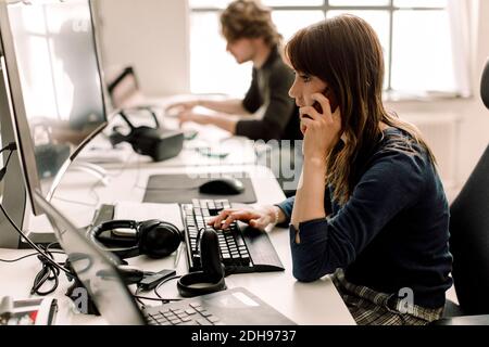 Female entrepreneur working on computer while talking on phone at workplace Stock Photo