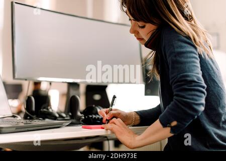Female computer programmer talking on smart phone while writing at workplace Stock Photo