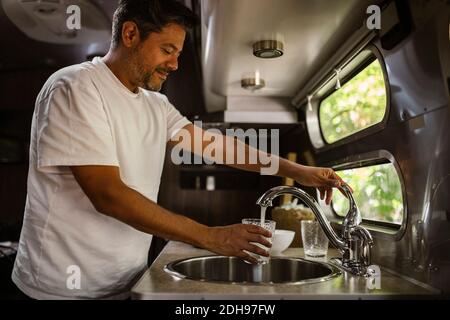 Smiling man filling drinking water through faucet in camper trailer Stock Photo