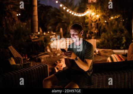 Smiling man using smart phone while sitting in garden during sunset Stock Photo