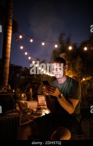 Smiling man texting while sitting outdoors during sunset Stock Photo