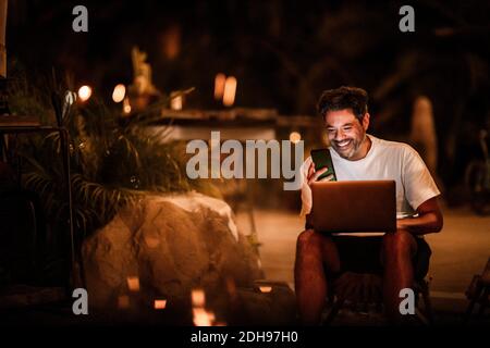 Happy man using phone and laptop at night Stock Photo