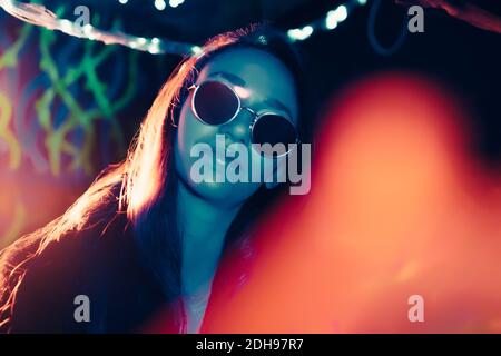 Portrait of confident young woman with illuminated reflection on sunglasses in restaurant Stock Photo