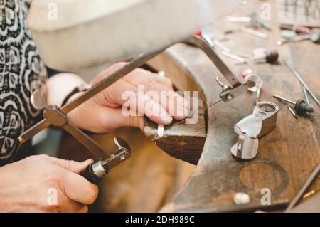Cropped image of senior woman cutting metal with hand saw in jewelry workshop Stock Photo