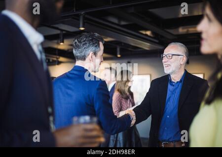 Male entrepreneurs shaking hands while standing in office Stock Photo