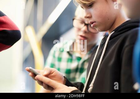 Middle school boy using mobile phone with friends in corridor Stock Photo
