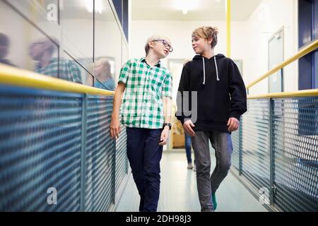 Boy talking with male friend while walking in school corridor Stock Photo