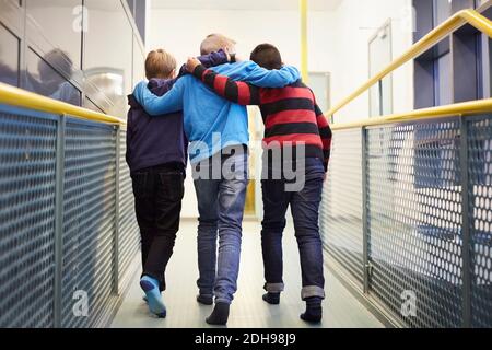 Full length rear view of boys walking arm around in school corridor Stock Photo