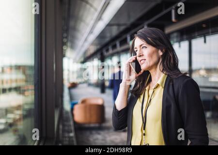 Female entrepreneur talking on smart phone while standing at workplace Stock Photo