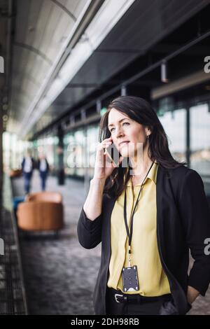 Female entrepreneur talking on mobile phone while standing at workplace Stock Photo