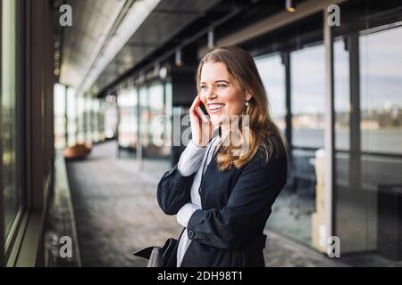 Smiling businesswoman talking on phone while standing at workplace Stock Photo