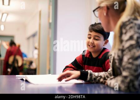 Mid adult teacher teaching boy at desk in classroom Stock Photo