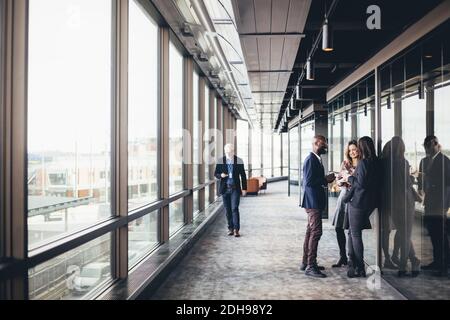 Smiling entrepreneurs talking while colleague walking in office corridor Stock Photo