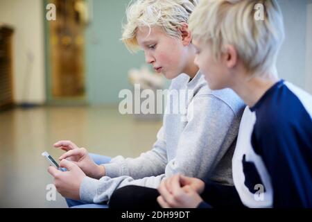 Boy looking at friend using mobile phone in school corridor Stock Photo