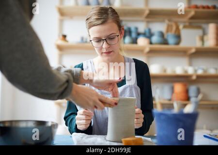Female teacher assisting young woman in making pot in art class Stock Photo