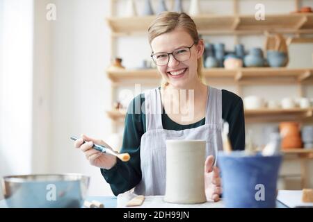 Portrait of smiling young woman learning pottery in art studio Stock Photo