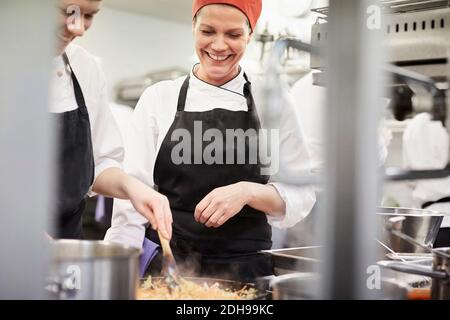 Teacher watching female chef student cooking food in kitchen at restaurant Stock Photo