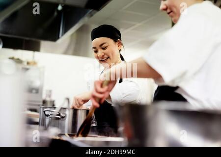 Smiling female chef student with colleague cooking food in commercial kitchen Stock Photo