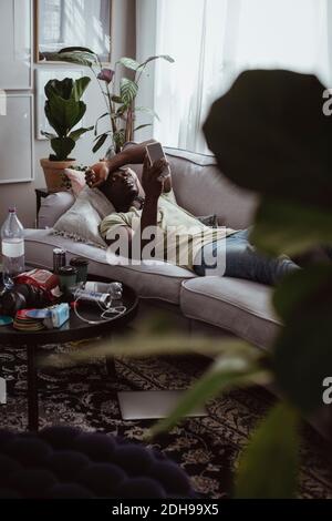 Sad man using smart phone while lying on sofa at home Stock Photo